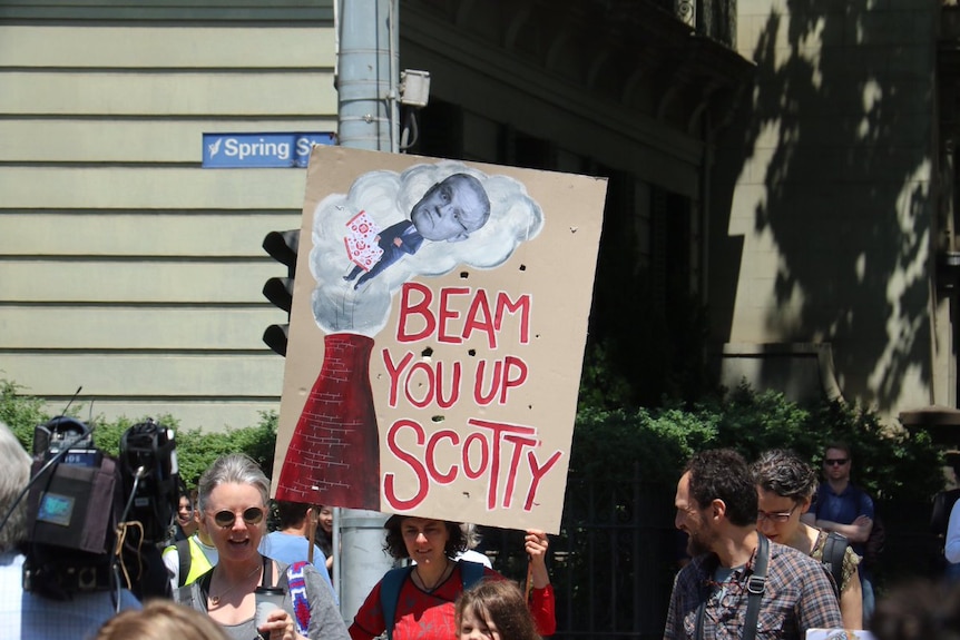 A woman holds up a protest sign saying 'Beam you up Scotty'.