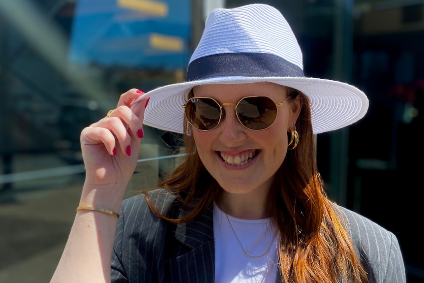 A woman wearing sunglasses and hat and touching the brim of it