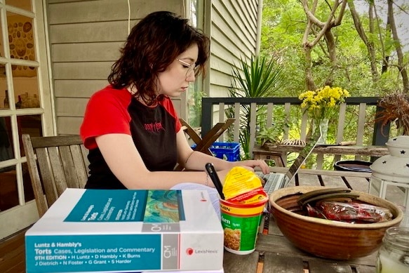 young woman sitting at a laptop with ramen noodlesa nd text books beside her