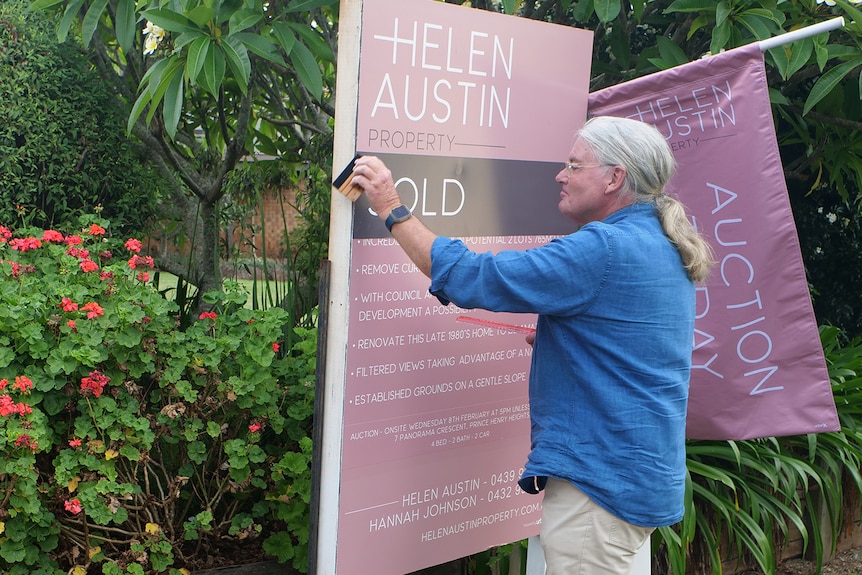 A man stick a sold sign on an auction board outside a house.