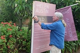 A man stick a sold sign on an auction board outside a house.