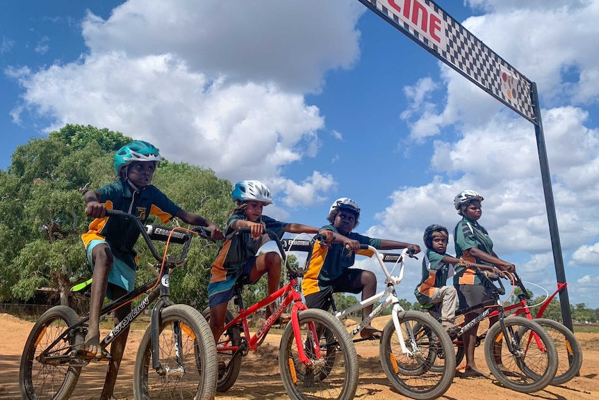 Five young people line up to start a BMX race under a banner that reads 'finish line'.