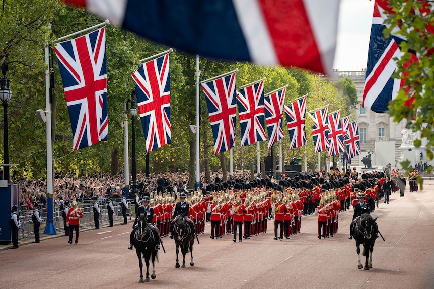 Horses lead the official procession and Union Jack flags line the road. 