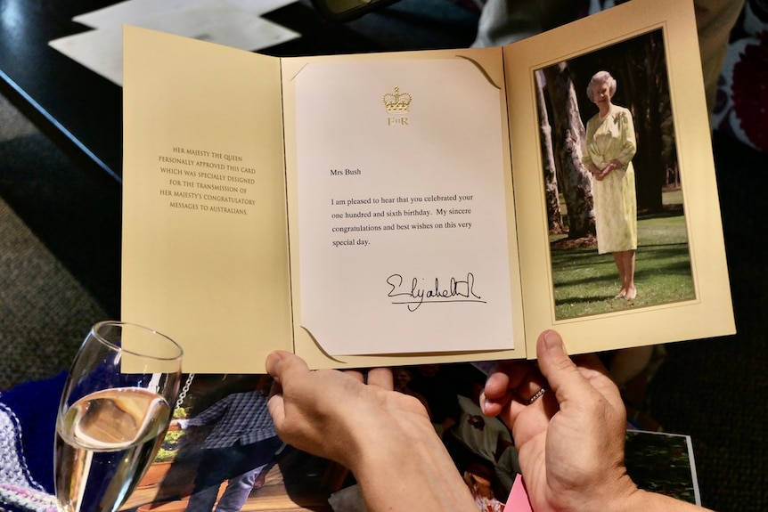 A woman holds a birthday card from the Queen, which includes a photo of the queen.