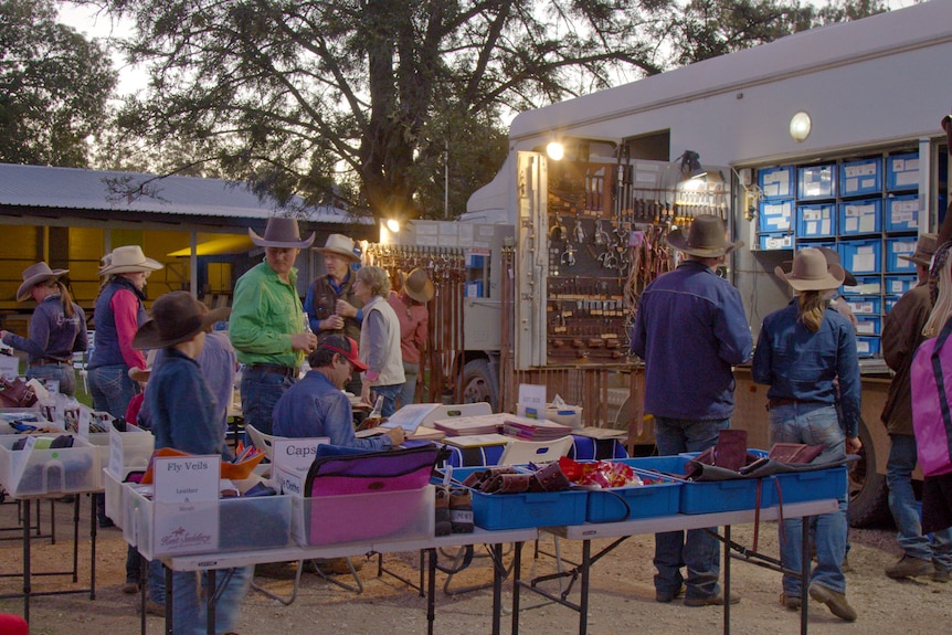 People standing around looking at products on tables next to a small truck