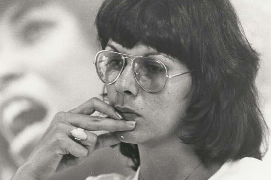 A black and white photo of Pat Turner as a young woman with large aviator glasses on. She has her hand up near her mouth.