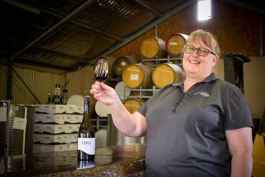 A woman holds up a glass of red wine.