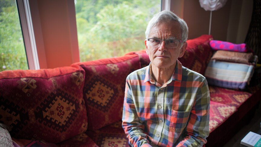 A man wearing a checked shirt sits on a red patterned couch