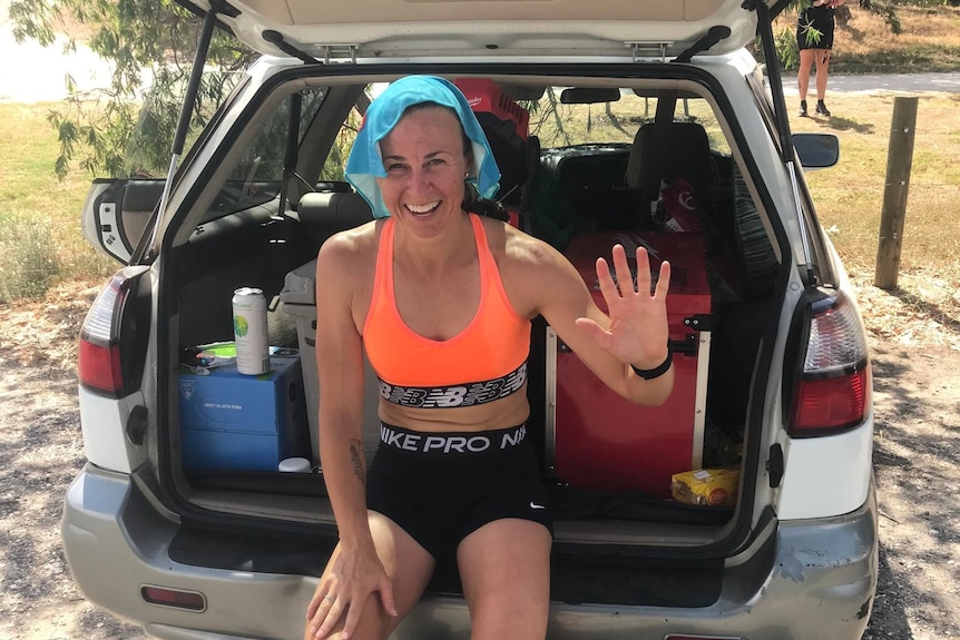 A woman sits in the car with a blue towel on her head to wipe away the sweat.