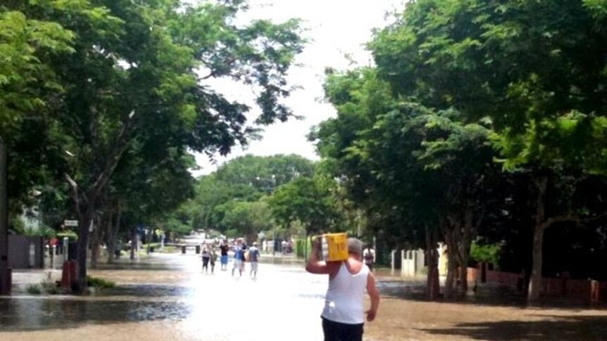A man carries a carton of beer through floodwaters at New Farm