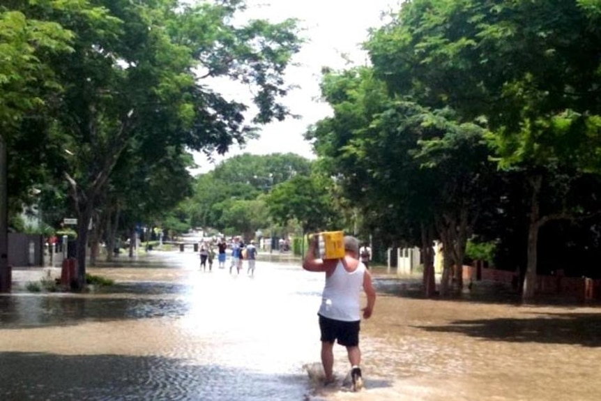 A man carries a carton of beer through floodwaters at New Farm