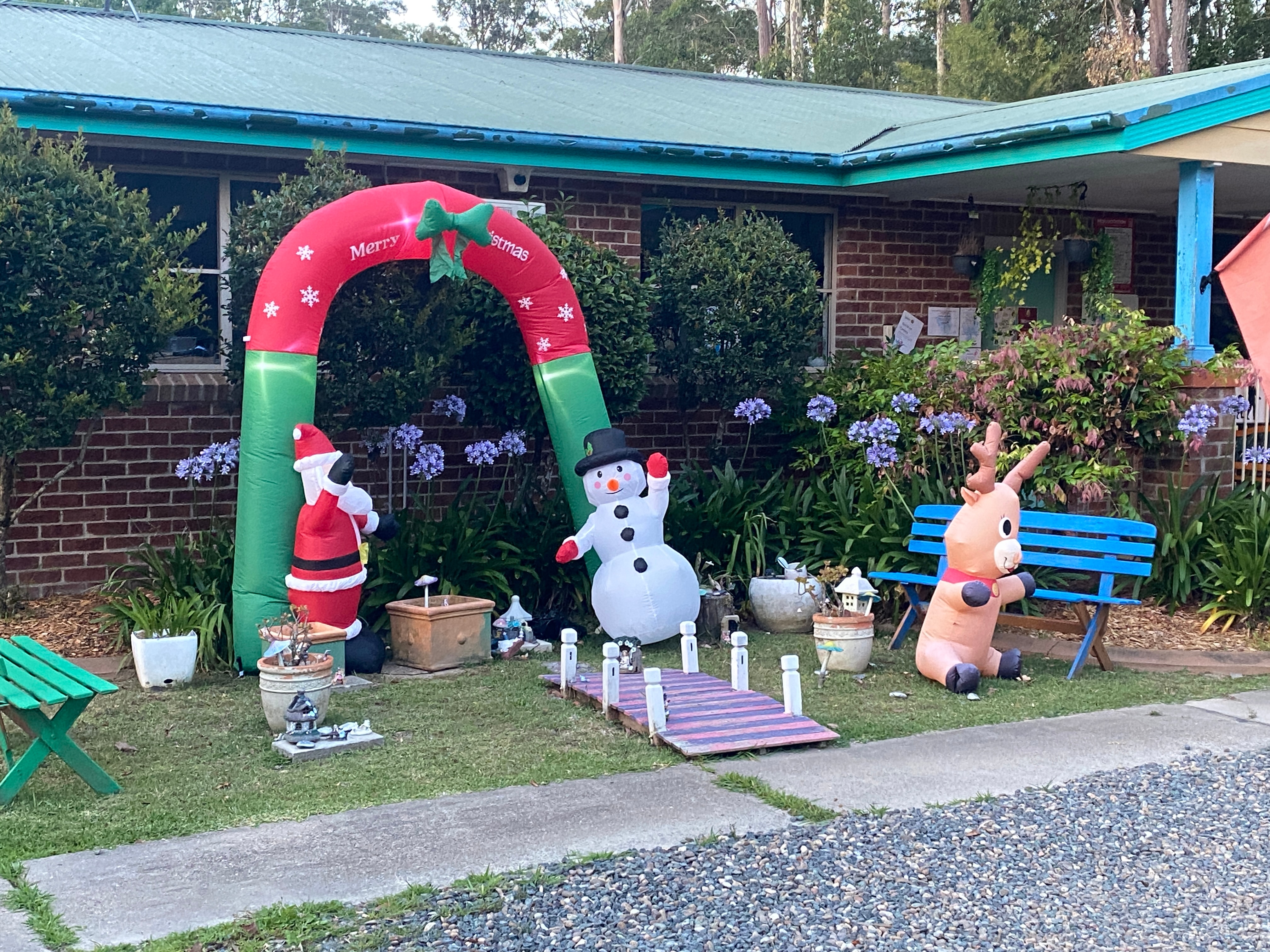 Uma casa de tijolos vermelhos com telhado azul e decorações de Natal, Papai Noel, boneco de neve e um laço vermelho e verde.