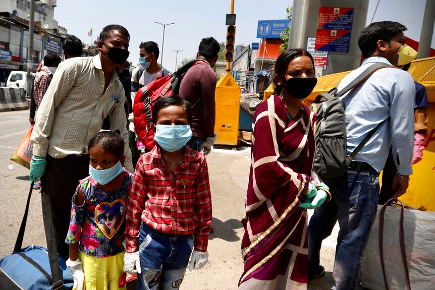 A man, a woman and two young children, all wearing masks, stand in a line on the street outside a train station