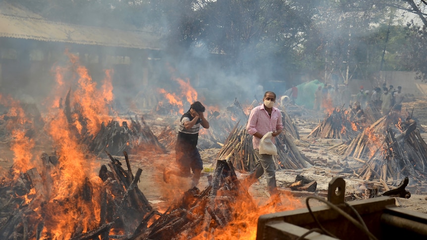People walk among flaming funeral pyres
