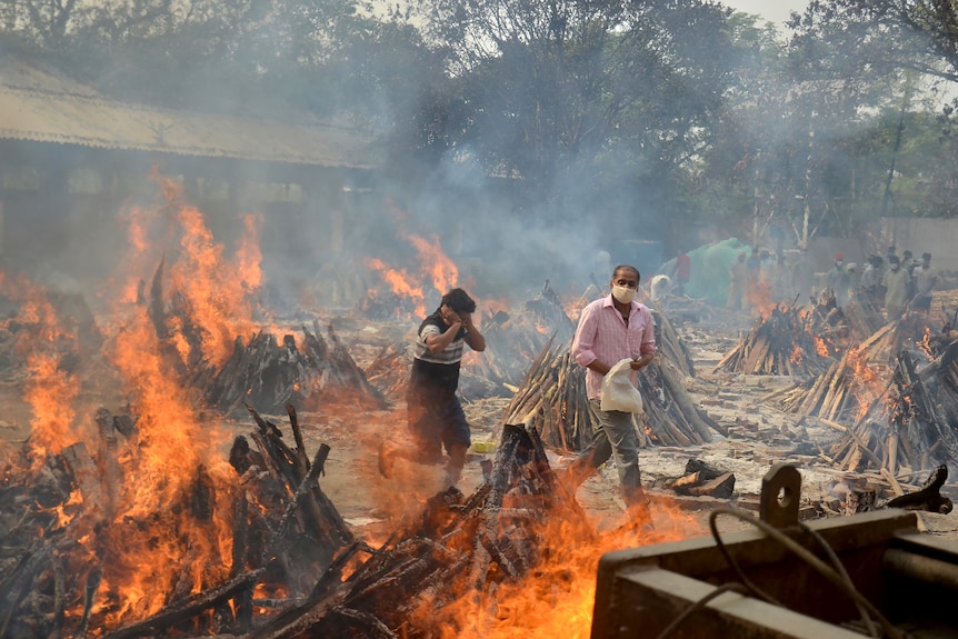 People walk among flaming funeral pyres