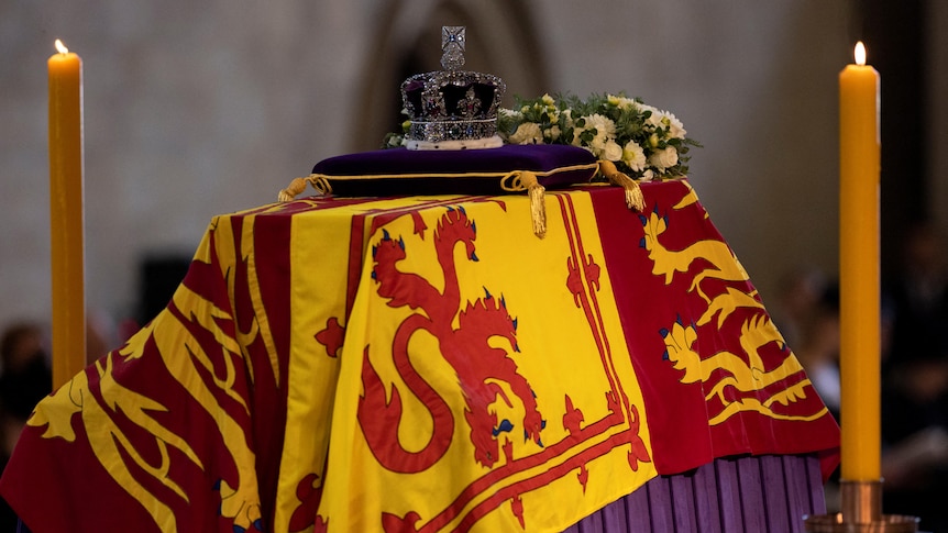 A coffin draped in a flag lies on top of a raised platform.