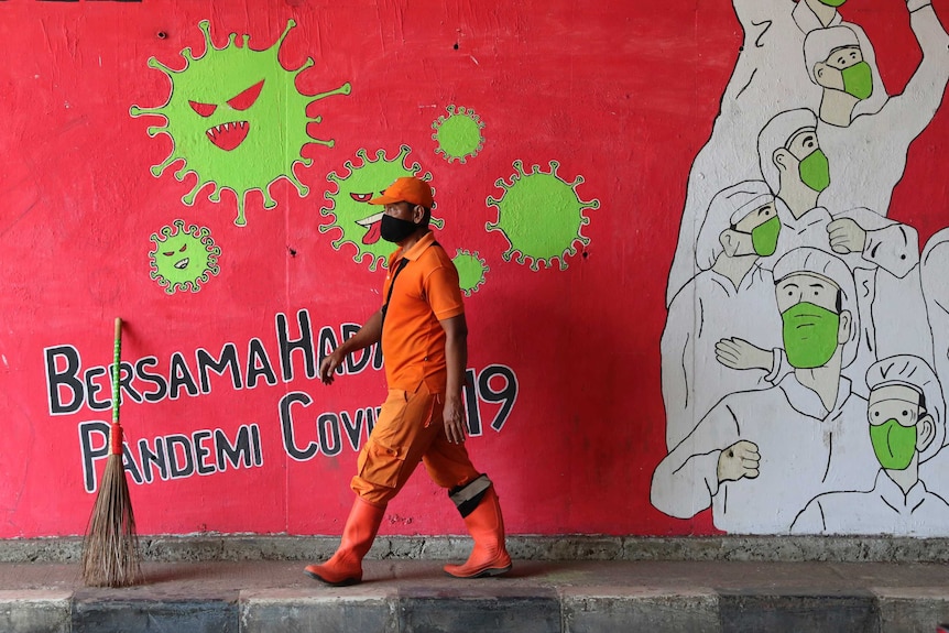 A street sweeper walks past a coronavirus-themed mural honouring health workers in Jakarta.
