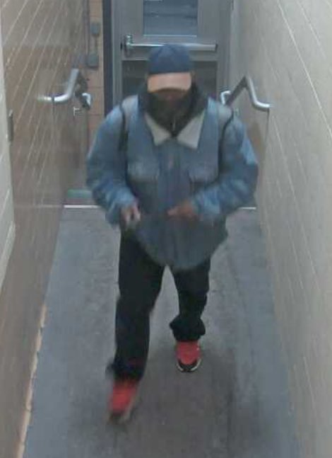 A man walks weaing a cap , a blue jacket and jeans. 
