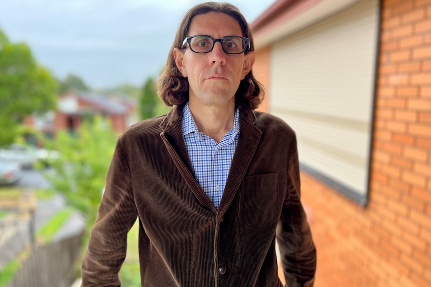 Jago Dodson stands near a red brick house wearing glasses