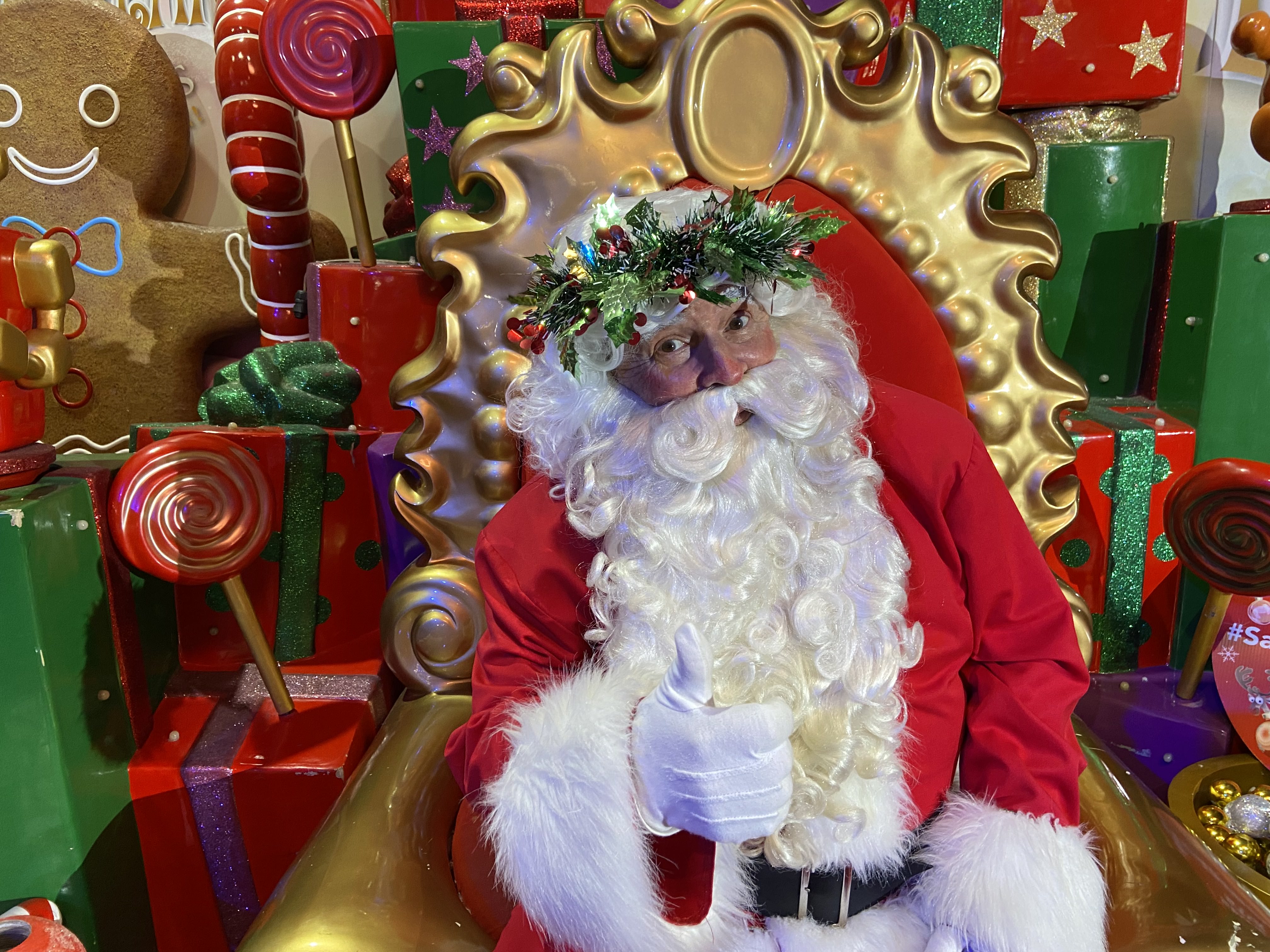 Un Papá Noel se sienta en un trono y sonríe a la cámara con el pulgar hacia arriba