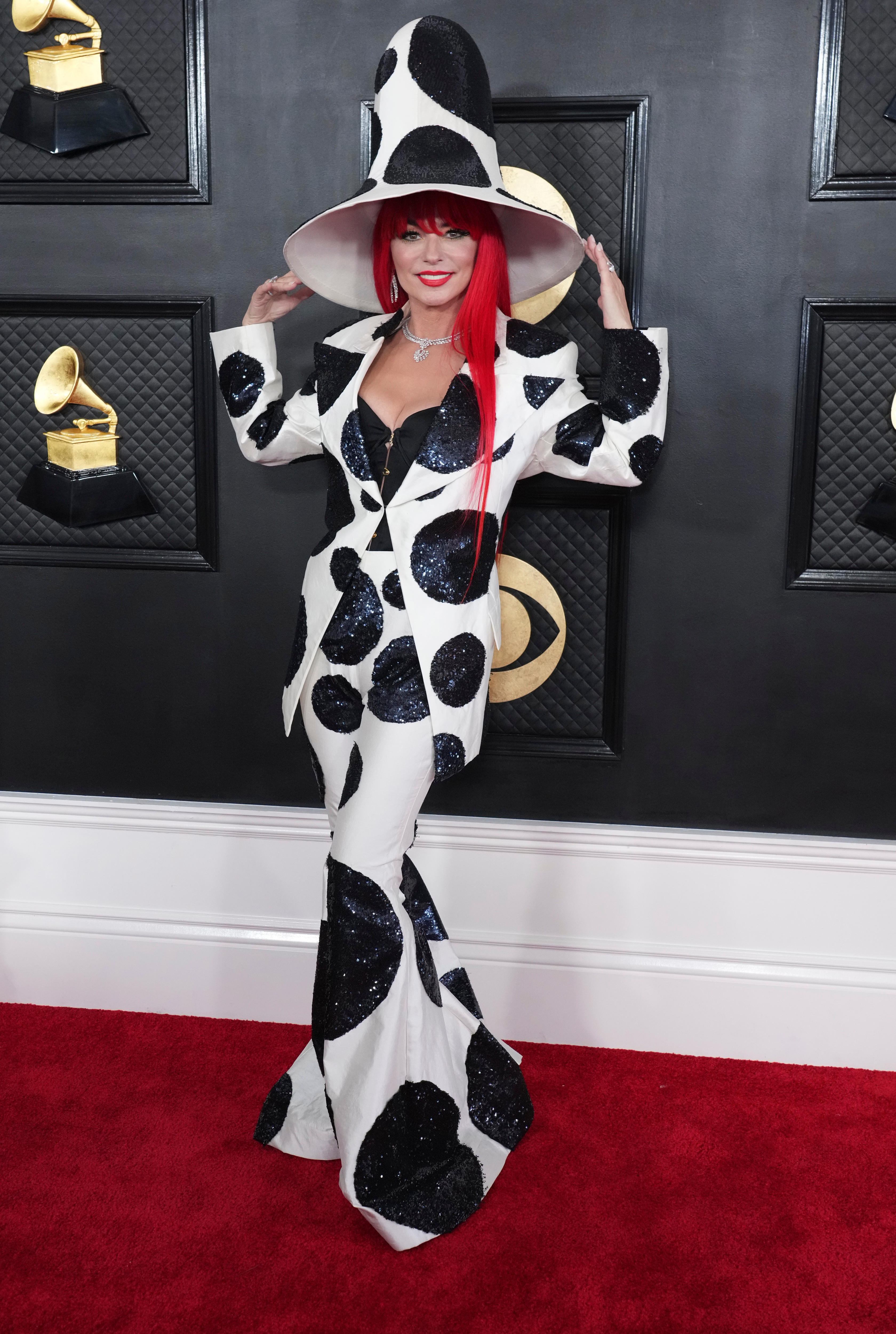 Shania Twain wearing a white, spotty suit with a matching hat and a bright red wig. 