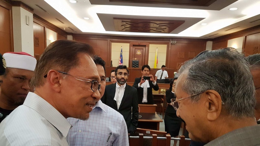 Anwar Ibrahim and Mahathir Mohamad speak in court while others look on.