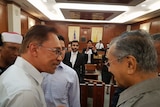 Anwar Ibrahim and Mahathir Mohamad speak in court while others look on.