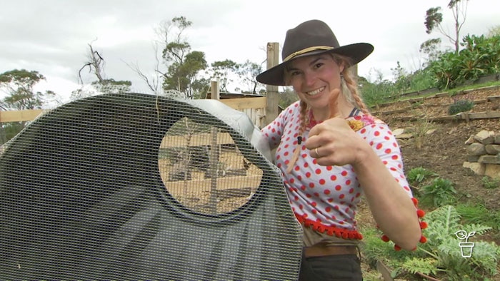 Girl wearing hat holding up a compost bin with wire mesh attached to the bottom