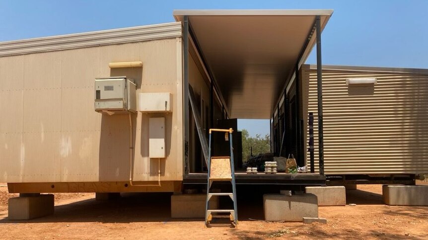 A ladder leaning on a container home structure with metal walls and a hallway through the middle.