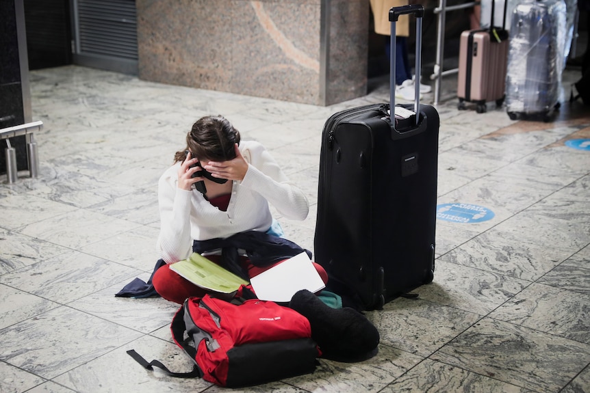 woman crumpled on her knees in an airport talking on the phone