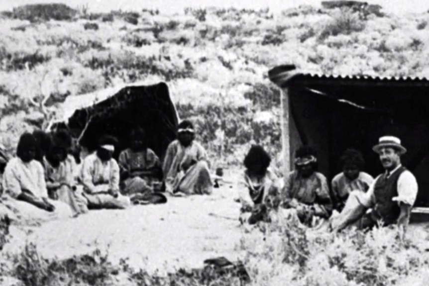 A black-and-white image of Aboriginal people sitting on sand dunes.