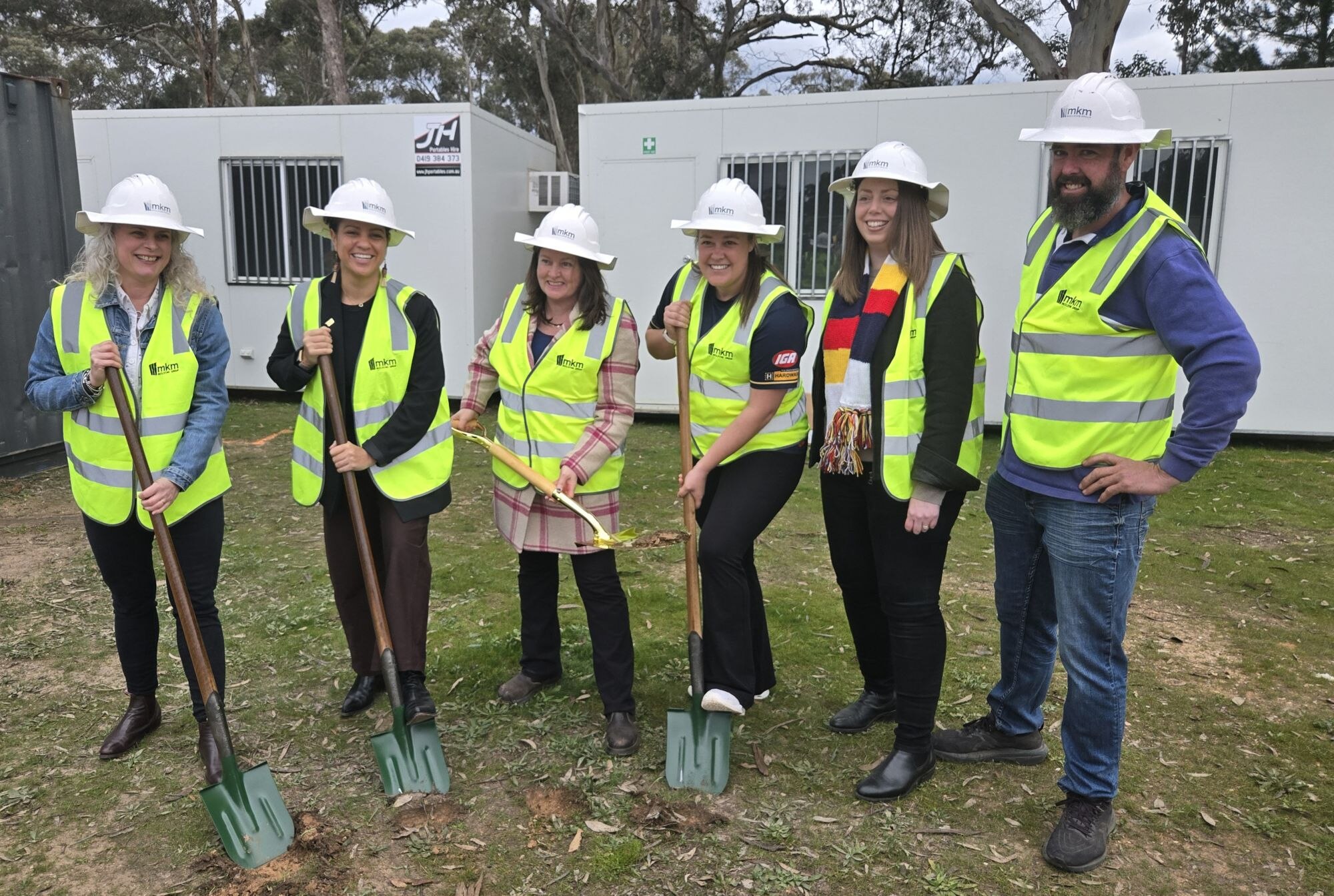 Photo of six smiling people posing as they turn the sod