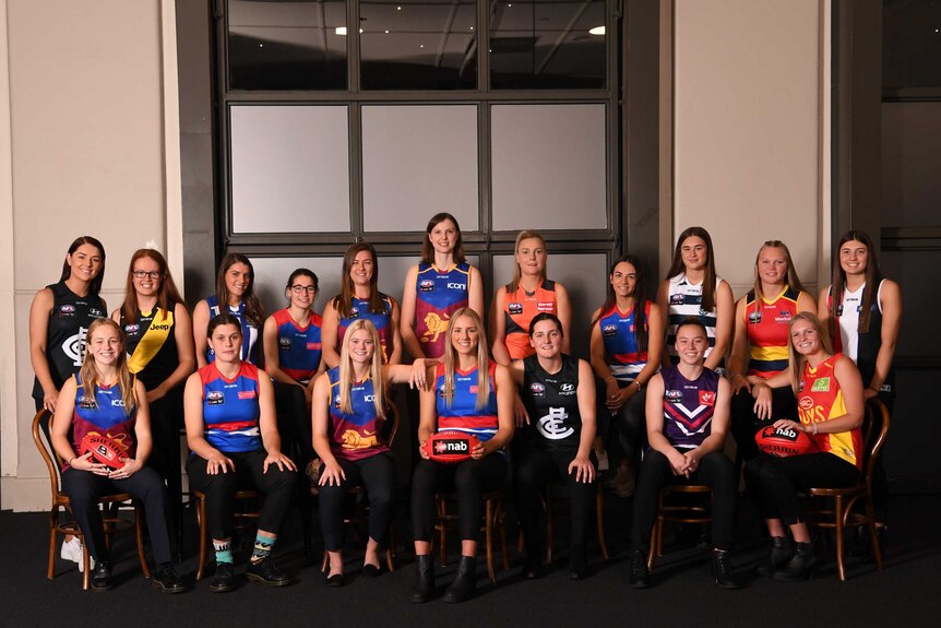 A number of footballers stand smiling in a group shot after round one of the AFLW Draft.