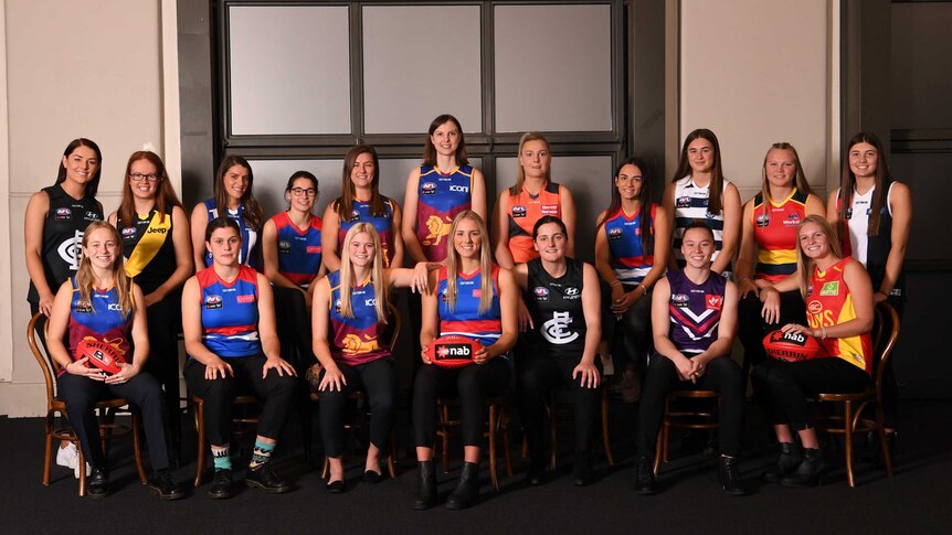 A number of footballers stand smiling in a group shot after round one of the AFLW Draft.