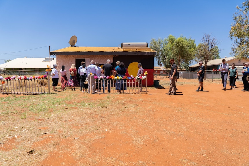 A group of people line up to enter a small home with an Indigenous flag painted on it