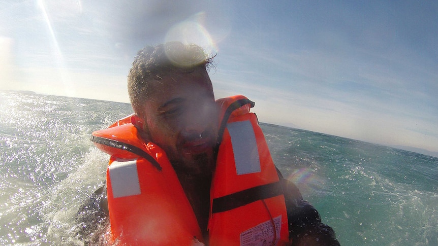 A man looks upset, wearing an orange lifevest as he is rescued in the ocean