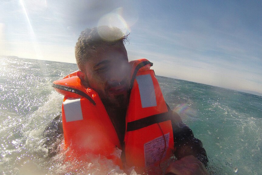 A man looks upset, wearing an orange lifevest as he is rescued in the ocean