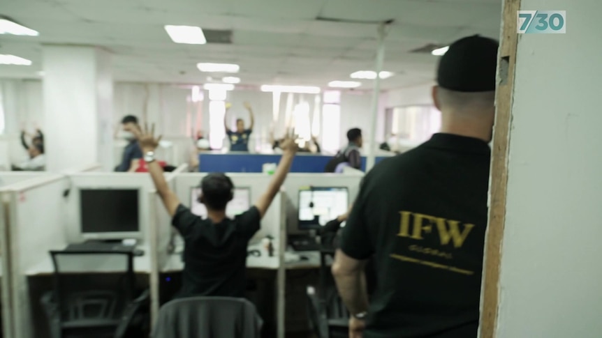 People at office desks hold their hands in the air.