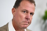 Alen Stajcic looks towards the camera wearing a beige suit jacket and white shirt