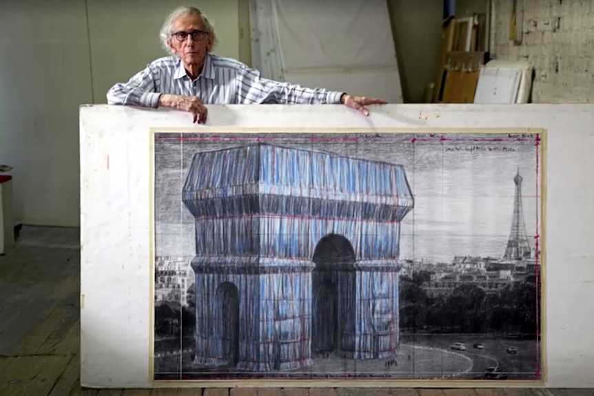 Man stands holding large sketching of Arc De Triomphe wrapped up 