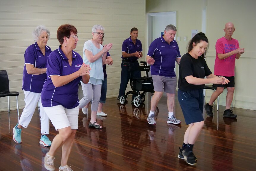 A group of older people follow a teacher through a dance routine