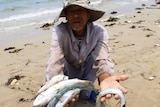 A man holds up dead fish on a beach in Vietnam.