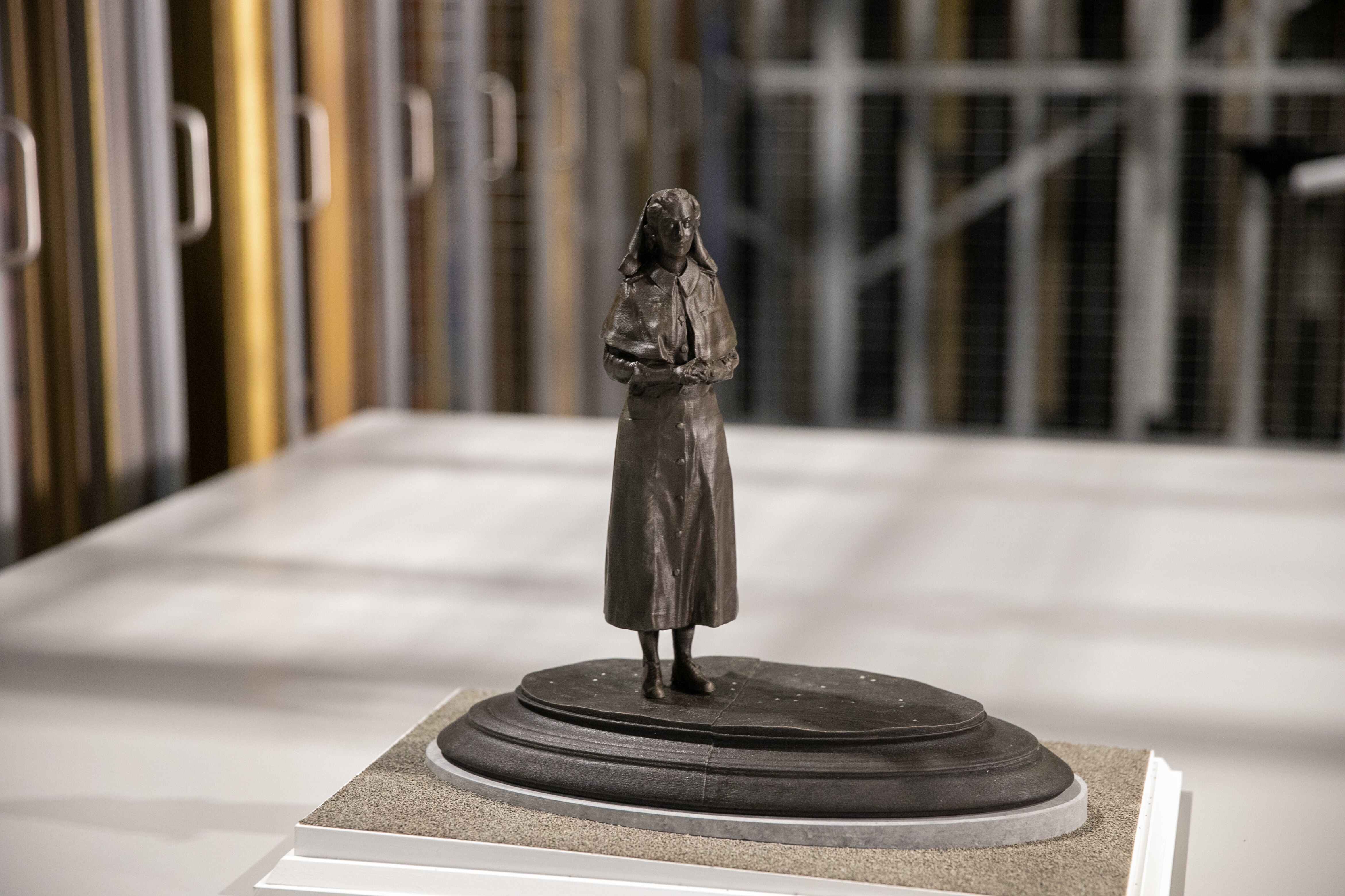 A small brown statue against a white background holding her hands together