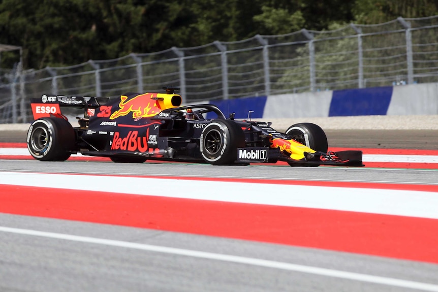 A side view of Max Verstappen's Red Bull car on red and white painted track.
