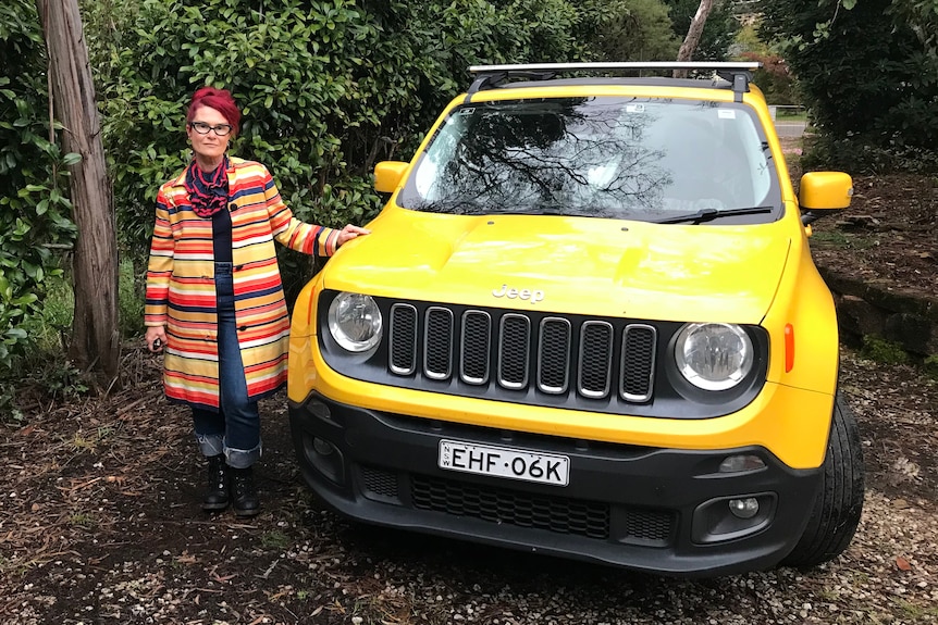 A woman in a striped coat stands next to a yellow car. 