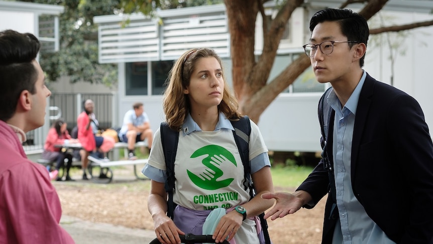 A girl with curly brown hair  wearing white and green shirt with a red pram and man wearing black glasses in a park