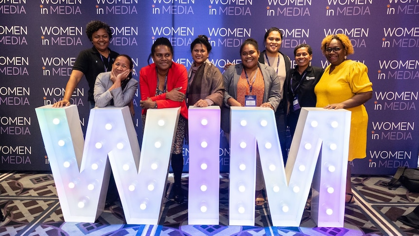 A group of woman standing in from of a WIM sign