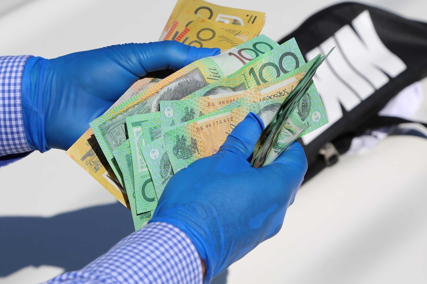 Gloved hands holding $100 and $50 banknotes.