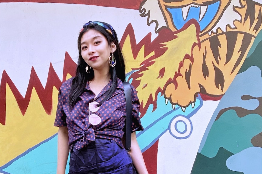 A young woman poses in front of a wall featuring a mural of a tiger.