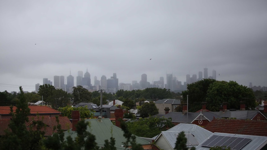 Melbourne's skyline is seen below a gloomy sky the tiled roofs of houses.